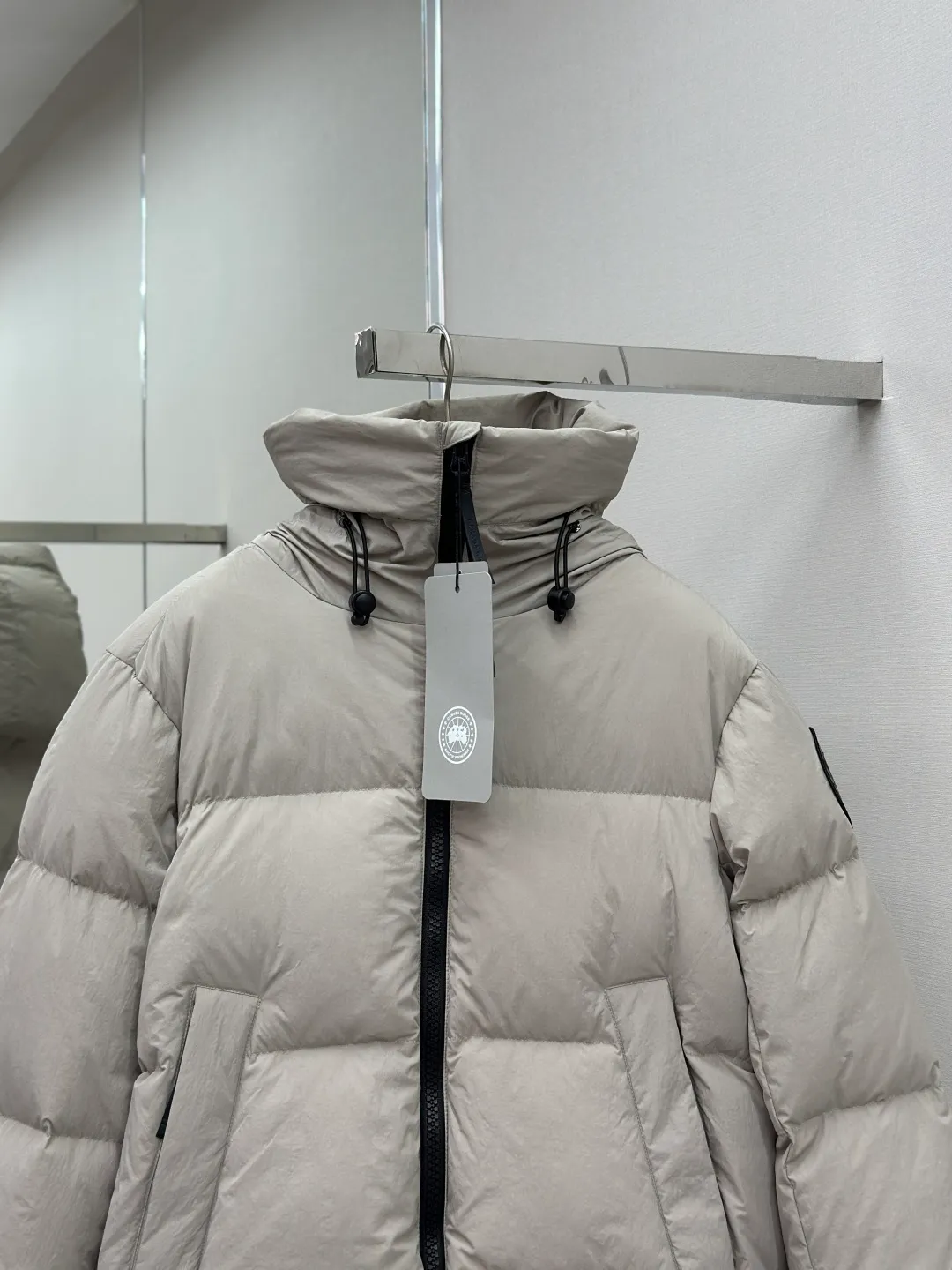 P1010 Canada Goose Black Label Badge Hooded Down Jacket (khaki) The high-quality filling is made of 90 national standard high-quality white duck down, selected high-loft velvet, weighing 240g, light and warm, with excellent temperature locking performance and good resilience. The fabric is woven with 400T high-count yarn. After special water-repellent treatment, the surface forms a lotus leaf effect - raindrops will slide down like beads, and snow particles will fall off when touched. The tear resistance reaches 200N (approximately 20kg load-bearing), the light gray matte texture breaks the stereotype of "outdoor clothing = hardcore", and the soft luster presents a high-end matte effect under urban neon lights, seamlessly switching scenes from ski resorts to CBD office buildings. The ribbon is woven with polyester as the base, and the brand letters are decorated on the ribbon through high-precision computer embroidery. The edges of the pattern are clear, the stitches are fine and even, and multiple layers of embroidery thread are stacked to enhance the three-dimensional effect. Precision thread reinforcement prevents linting and ensures the fluffy and resilient elasticity lasts as new. The embedded cuffs are three-dimensionally woven to form a "wavy" elastic structure, which forms natural folds when fitting the wrist, increasing the contact area with the skin, thus improving the windproof effect. At the same time, micro-velvet treatment is added to the inside of the cuffs, which feels like a second layer of skin and avoids friction on the skin from metal zippers or hard fabrics. Size:S-M-L-XL